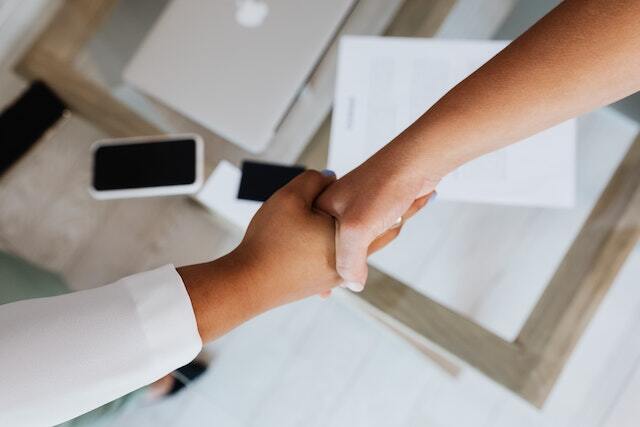 Two people reaching across a desk to shake hands